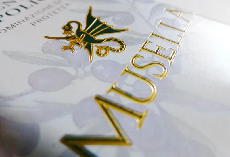 Etichetta Musella con oro a caldo e rilievo su carta chiara, logo drago alato e dettagli grafici naturali – progetto Win